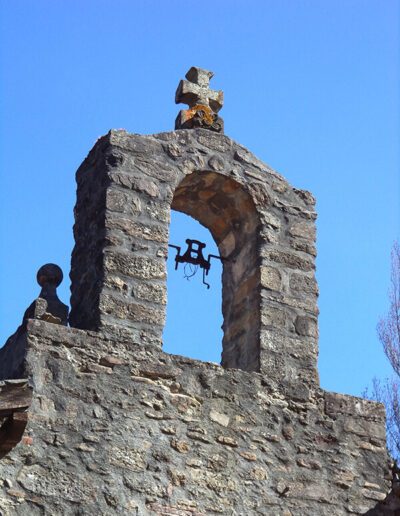 La espadaña está decorada con una cruz y una flor tallada.